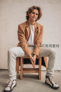 卷发青年坐木凳，驼色西装显随性