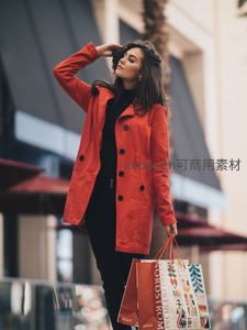 红色风衣女子手提购物袋街头漫步
