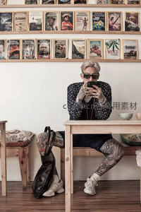 纹身青年在杂志墙前专注玩手机