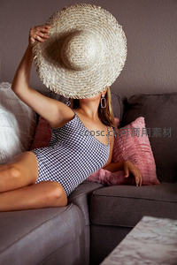 草帽遮面女子慵懒倚沙发，格纹泳衣显清凉