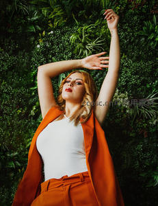 橙色套装女子绿植墙前伸展