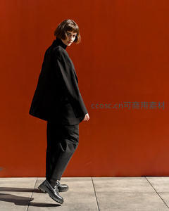 黑衣短发女侧身回眸，红墙为幕