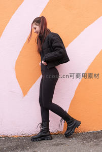 橙粉墙前黑衣女子侧身微笑