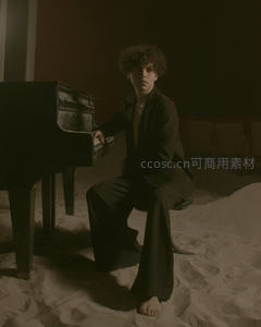 沙地钢琴旁卷发少年静坐凝视