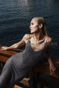 深色礼服女子倚船舷凝望