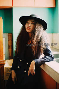 卷发美女戴宽檐帽，慵懒倚靠展复古风情