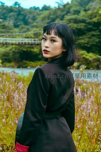 黑衣女子回眸立于河畔花丛之中