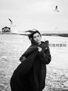 海边寒风中女子裹紧大衣，海鸥翱翔
