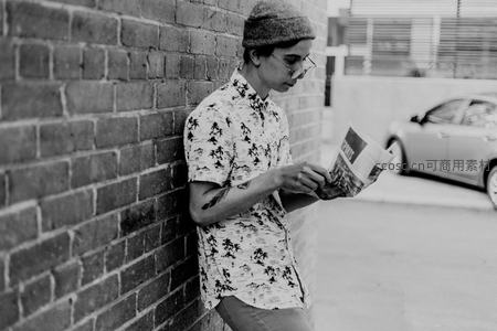 青年靠墙阅读报纸，街头文艺气息