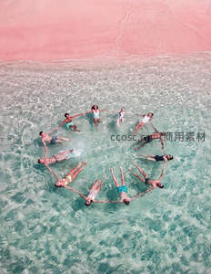 粉红沙滩碧海中，众人手拉手围成爱心形状