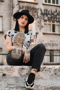 纹身女孩戴帽坐于涂鸦墙前