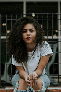 卷发少女凝视镜头，背景铁网朦胧