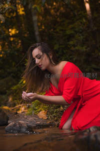 红裙女子溪边掬水，林间光影斑驳