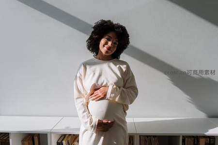 阳光下的温柔孕妈，手抚腹部微笑