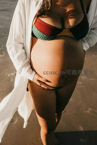 海滩阳光下孕妈特写，手护孕肚温暖自然