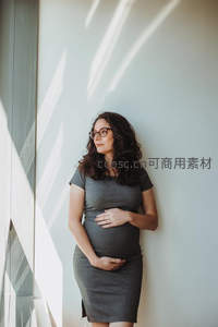 戴眼镜的孕妈靠墙凝望，阳光洒落如诗