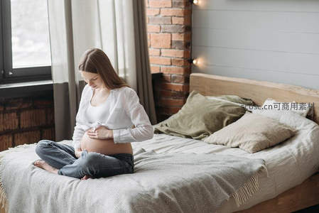 孕妈床前凝视孕肚，砖墙暖灯相伴