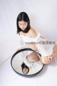 孕妈俯身镜前，白色纱裙映衬温柔母爱