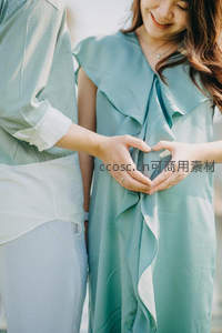 情侣携手比心，浅绿裙装映衬幸福孕期
