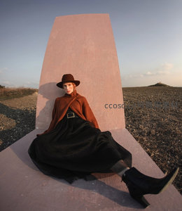 粉墙前戴帽女子静坐田野