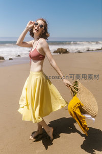 沙滩上欢笑的女子，手提草编包享受阳光