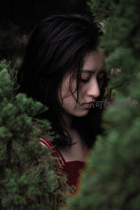 红衣少女藏身绿植间的侧颜特写