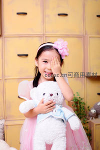 小女孩怀抱泰迪熊，头戴粉色花饰微笑
