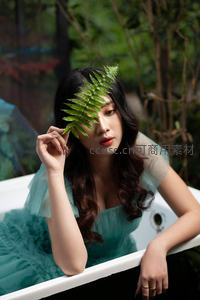 浴缸中女子手持绿叶遮眼凝视