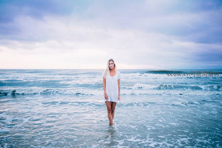 白衣少女伫立海浪轻抚的浅滩之上