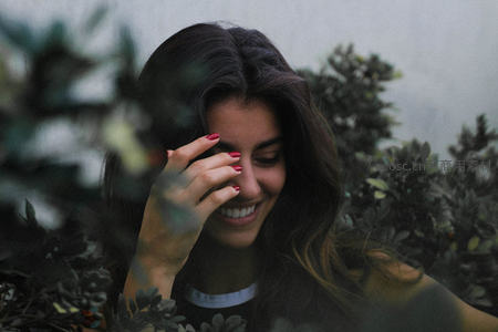 绿植掩映下微笑的女子，红指甲轻触面颊