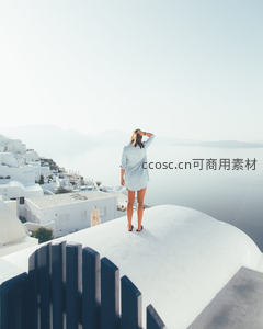 白衣女子伫立圣托里尼白墙之上远眺爱琴海