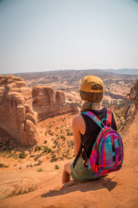 背包客坐于红岩之上远眺荒漠峡谷