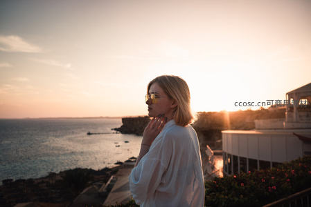 夕阳下白衫女子凭栏眺望蔚蓝海岸