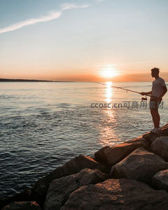 夕阳西下男子立于礁石垂钓海面