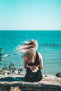 海风拂面，金发女子静坐石墙眺望碧海
