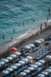 黑沙滩上蓝伞如花，游客戏水享夏日海滨