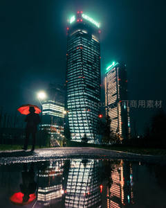 雨夜撑伞人影映衬摩天楼