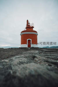 低角度仰拍橙色灯塔，岩石质感粗犷