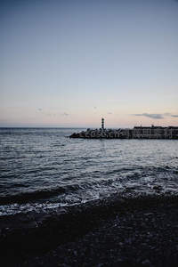 暮色海港灯塔孤影，浪花轻吻黑沙滩