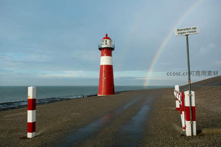 彩虹横跨红白灯塔旁警示路牌