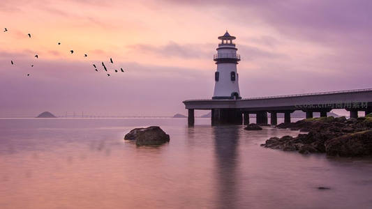 暮色灯塔映霞光，飞鸟掠过海天间