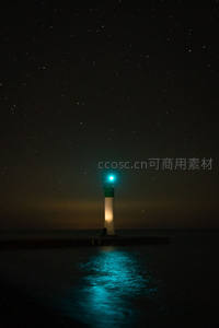 星空下的绿光灯塔映照水面