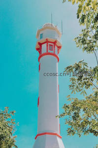 红白相间灯塔矗立蓝天绿树间