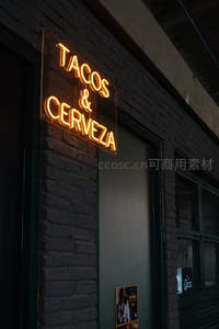 暖黄霓虹‘TACOS & CERVEZA’招牌，砖墙餐厅入口特写