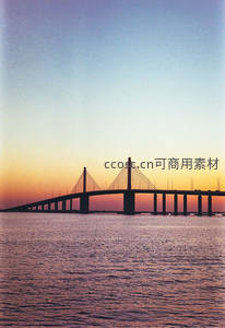 斜拉桥剪影映晚霞，海面波光如金绸