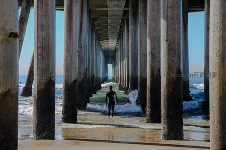 冲浪者穿行于码头支柱间的光影