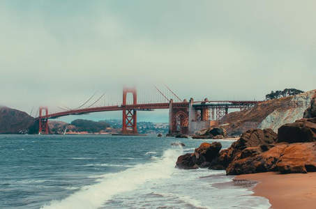 金门大桥在薄雾中若隐若现，海浪轻拍岩石海岸