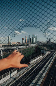 透过铁丝网拍摄现代都市摩天楼群与铁路