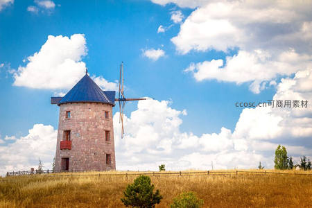 蓝天白云下的石砌风车矗立在金黄草地上