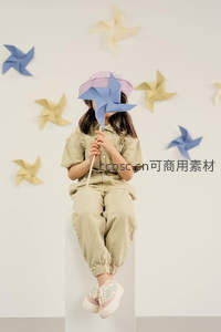 小女孩手持纸风车遮面微笑